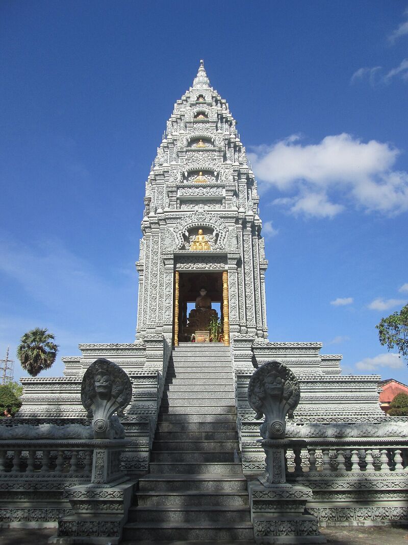 A tall white tiered stupa with naga balustrades on a stairway, under a blue sky.