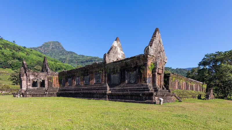 A long ruined sandstone building with tall gables on a lawn, with a mountain behind.