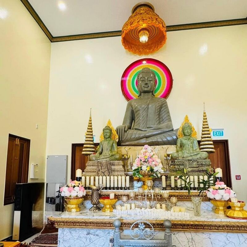 A large seated stone Buddha flanked by two smaller Buddhas on a gilded altar with flowers and candles.