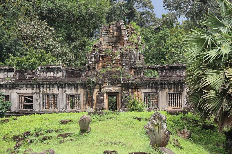A long weathered sandstone building with a central tower and rows of windows, behind green grass with carved stone figures.