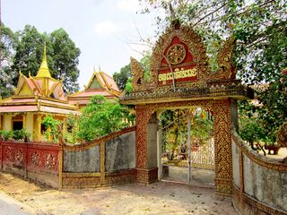 An ornate red and gold gateway in a low wall, with a temple roof beyond.