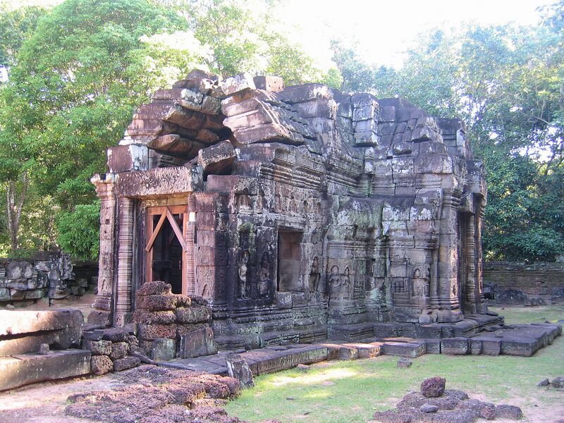 A small ruined sandstone sanctuary with a doorway, surrounded by trees.