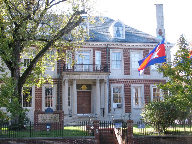 A red brick building with white columns at the entrance and a Cambodian flag flying in front.