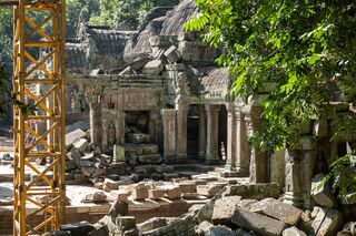 Yellow metal scaffolding standing among fallen stones beside a temple gallery.