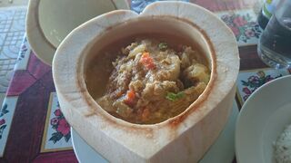 A halved coconut shell holding a creamy fish curry with herbs, on a restaurant table.