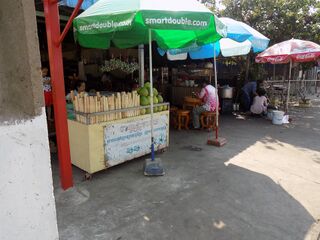 A roadside stall with upright bamboo tubes of kralan on a yellow cart under green and blue umbrellas.