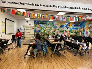 Adults and young people at tables in a classroom decorated with a mural and strings of flags.