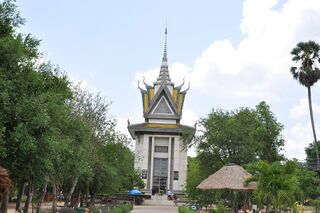 A paved path through trees and lawns leading to a tall white stupa with a tiered roof.