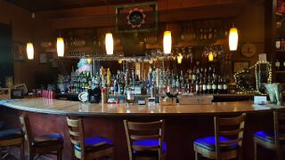 A curved bar with stools, warm lights and shelves of bottles.