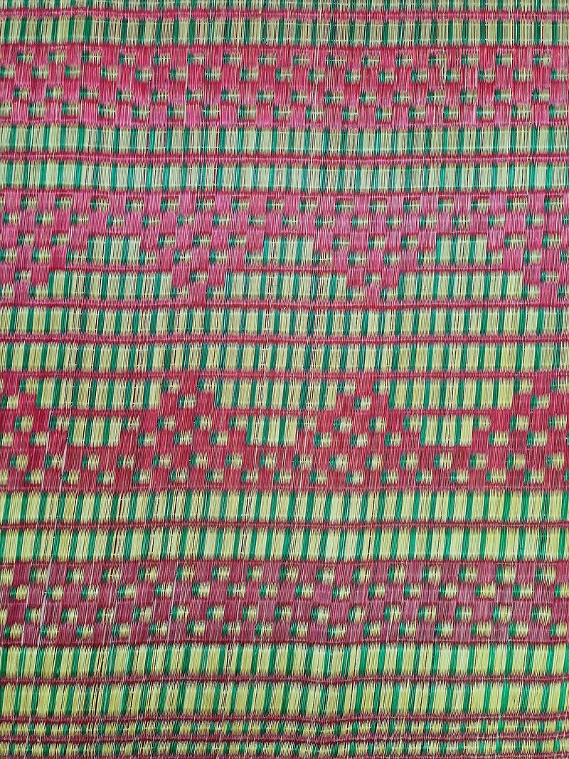 A close view of a woven mat in red, green and natural gold strips forming rows of diamond and triangle patterns.