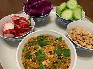 A bowl of minced pork dip with herbs surrounded by small bowls of radish, red cabbage, cucumber and peanuts.