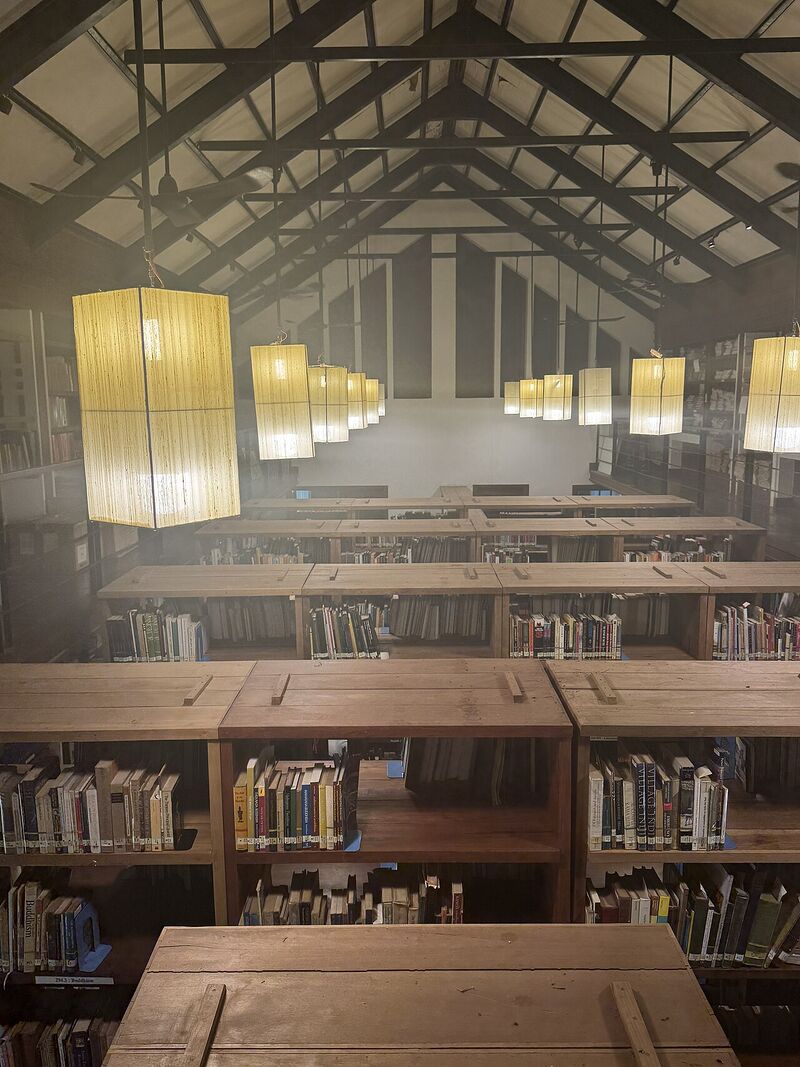 Rows of wooden bookcases filled with books under a timber roof hung with tall paper lanterns.