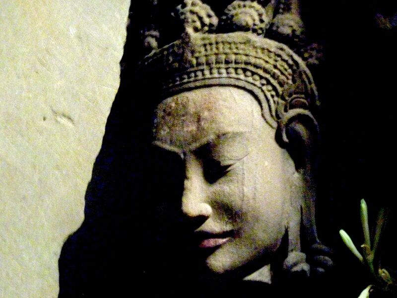 A carved stone face with a tall crown, shown in strong shadow