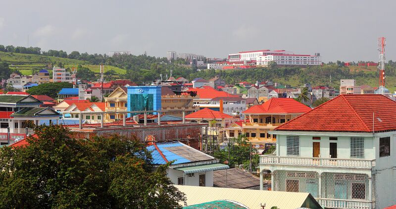 Rooftops of colorful houses and low buildings spread over a green hillside.