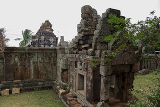 A stone gallery wall with window openings and a crumbling tower behind it.