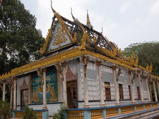 A temple hall with gilded eaves and painted panels, its roof stripped to a bare frame of beams.