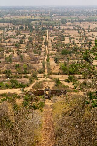 A long straight stone stairway descending a hillside towards flat farmland stretching to the horizon.