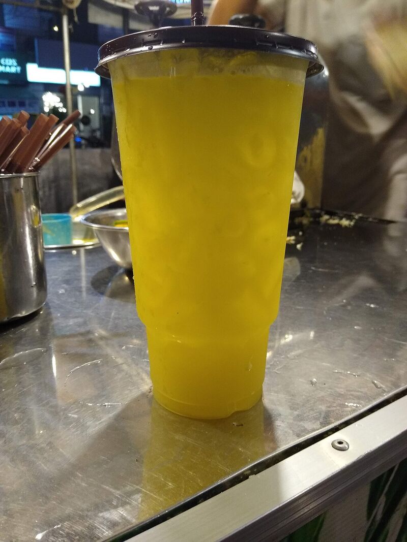 A tall clear cup of bright yellow-green sugarcane juice on a steel counter.