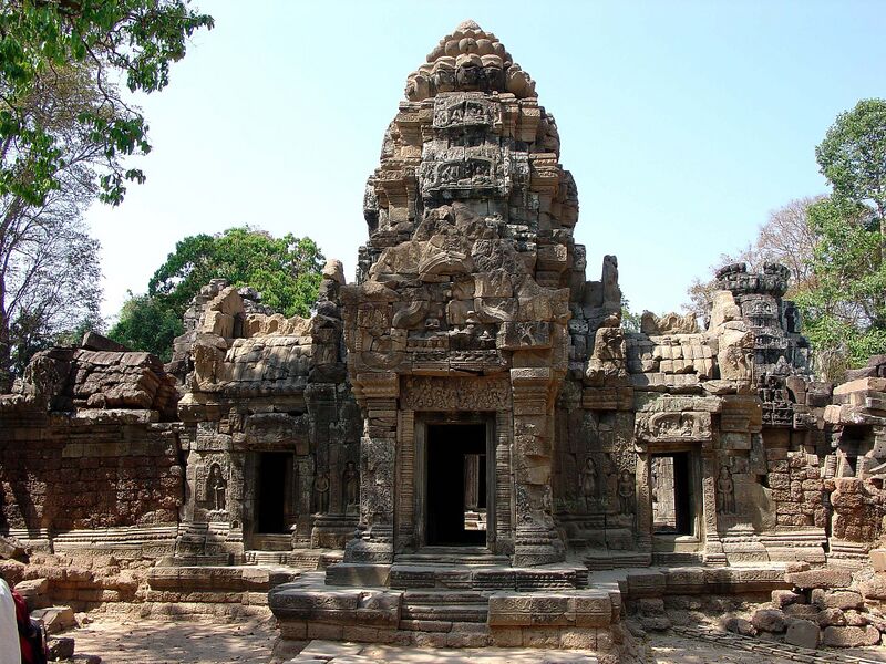 A carved sandstone tower above a doorway with lower side wings, with trees behind.