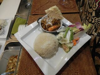 A white plate with rice, a small bowl of prahok ktis topped with a cracker, and raw vegetables.