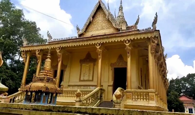 A gold-painted temple hall with a tall carved gable and decorated columns under a blue sky.