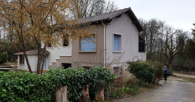 Two-storey rendered house with blue shutters behind a hedge and bare trees, with a driveway on the right.