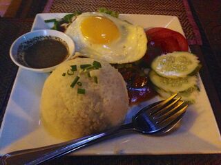 A plate with a dome of rice, a fried egg, sliced tomato and cucumber, and a small dish of dipping sauce.