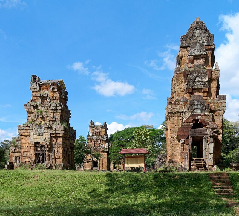 Tall square laterite towers standing in a grassy field under a blue sky.