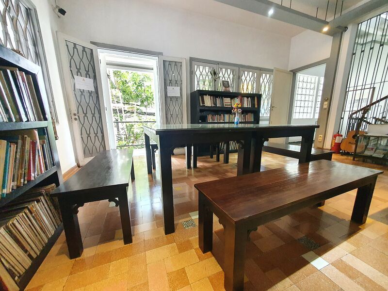 A bright room with wooden reading tables and benches, tall bookshelves along the walls and windows with patterned grilles.