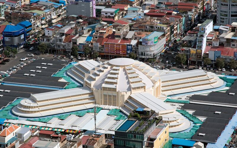 A cream-colored Art Deco market building with a central dome and four long wings spreads across a city block, surrounded by parking areas, rooftops and streets.