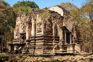 A square brick temple with decorated walls among tall trees.