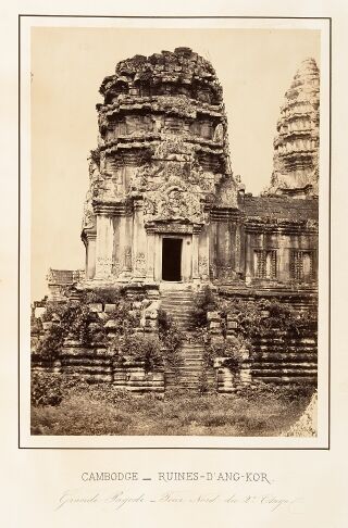 A carved stone tower with a doorway, rising above broken walls and rubble, with a second tower behind it.