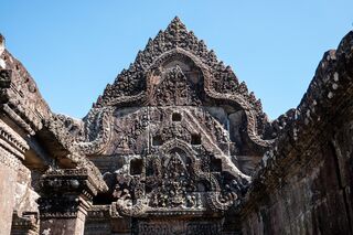 A triangular sandstone pediment densely carved with figures and scrolls against blue sky.