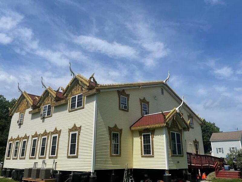 A two-storey cream clapboard building with gilded Khmer gables and red roof sections under a blue sky.