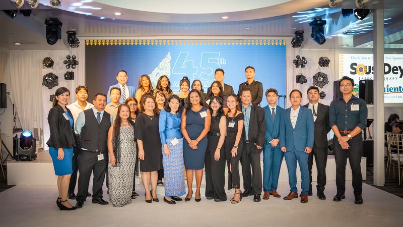 About thirty staff and board members in formal wear pose on a stage in front of a screen reading 45th Anniversary.