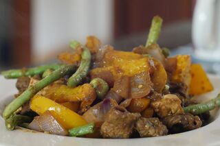 Pieces of beef, yellow pepper, onion and green beans coated in spice paste on a white plate.