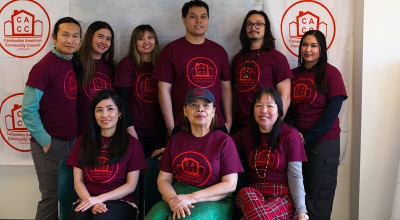 A group of adults in matching maroon shirts posing in front of a wall with the council's logo.