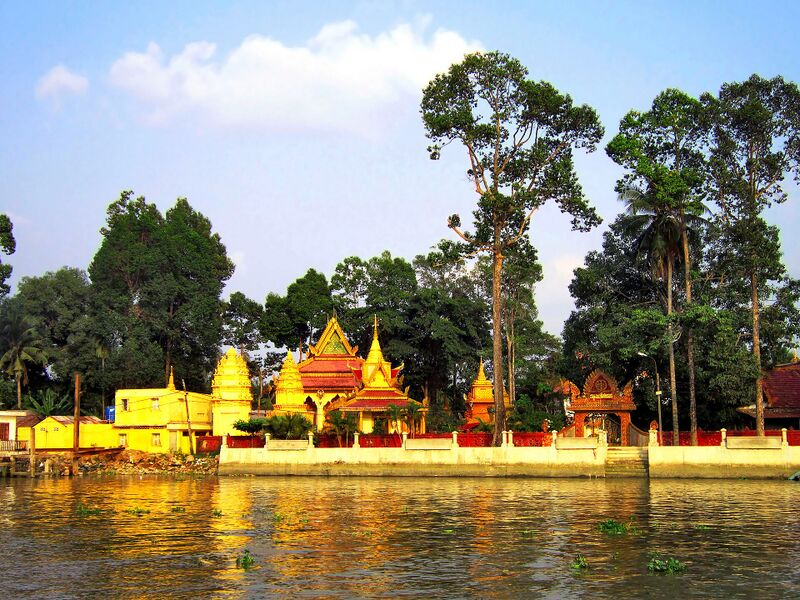 Yellow and gold temple buildings beside the water, with tall trees.