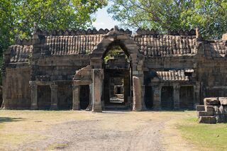 A long laterite enclosure wall with a central gate pavilion and a doorway, behind open ground.