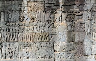 A gray sandstone wall carved with rows of small figures in procession.