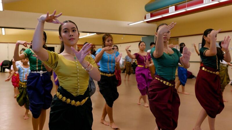 A row of dancers in colorful sampot and blouses practicing classical hand gestures in a large hall.