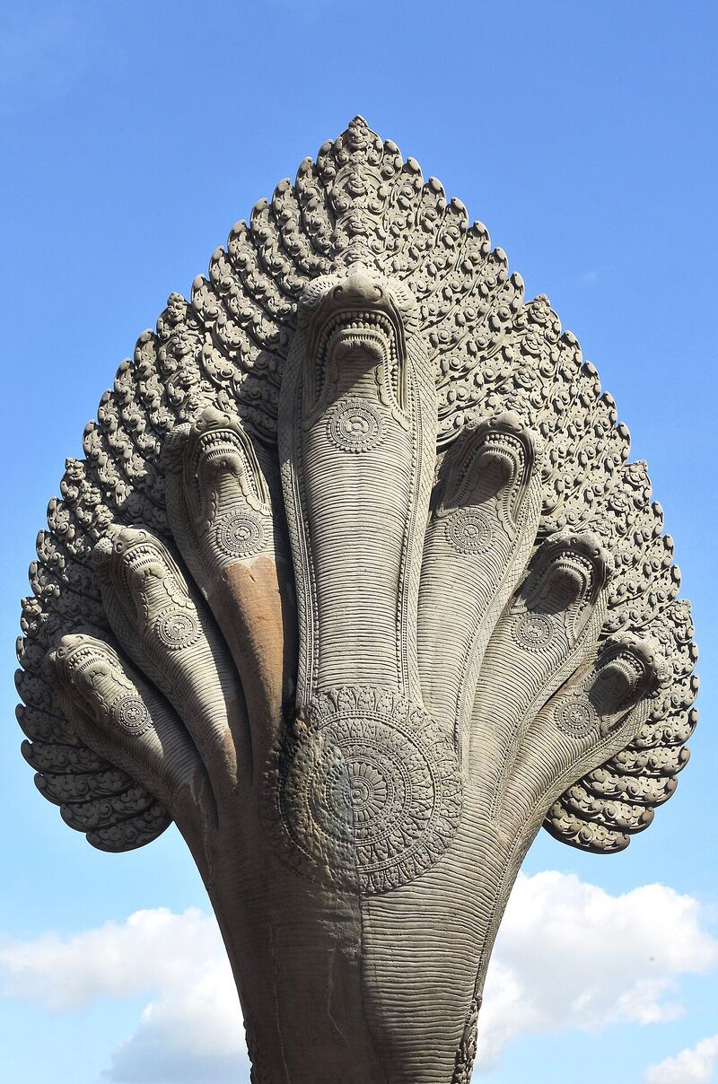 A carved stone serpent with seven hooded heads fanned out against a blue sky, rising from the end of a balustrade.