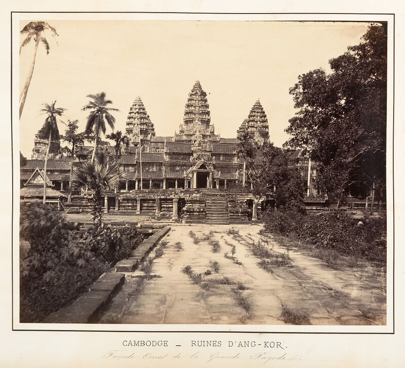 Angkor Wat seen from the stone causeway, with four of its towers rising behind the long entrance gallery, the leftmost partly hidden by palm trees.
