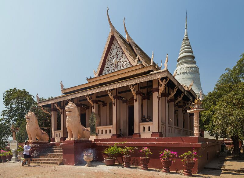 A temple with a tiered roof and carved pediment on a hilltop, with a tall white stupa rising behind it.