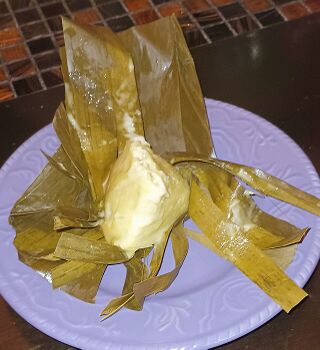 A soft pale rice cake on opened banana leaves on a lilac plate.