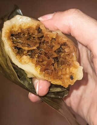 A hand holding a halved cake showing a brown coconut and sesame filling inside chewy white dough.