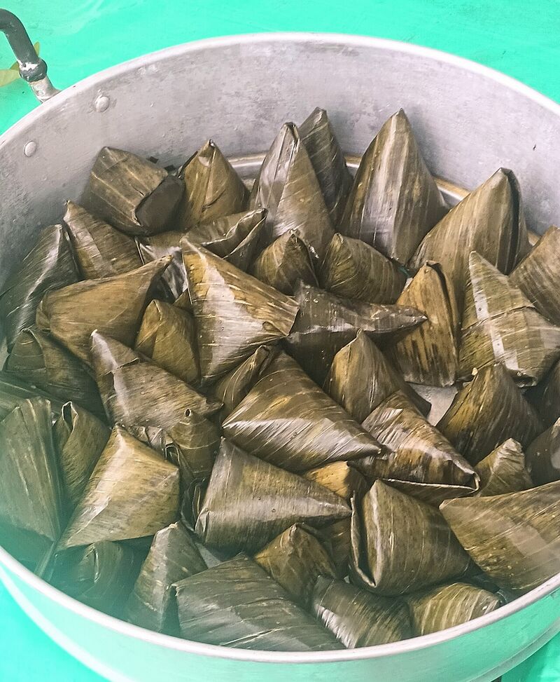 A steamer pan packed with dozens of pointed banana-leaf pyramids.