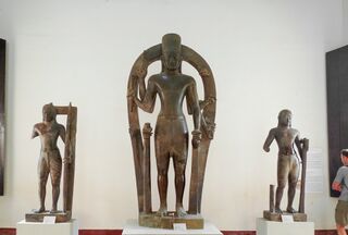 Three standing sandstone statues on plinths, a large eight-armed figure in the center.