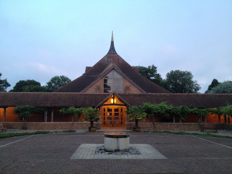 A brick temple with a steep pyramid roof and a gold spire seen across a paved courtyard at dusk.