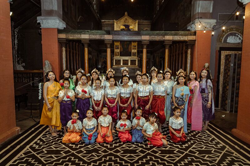 A group of girls and women in colorful Cambodian traditional dress posing in a hall with red pillars.